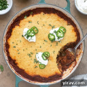Chili cornbread casserole in a cast iron pan with a spoon scooping a portion, showcasing the rich chili and fluffy cornbread layers.