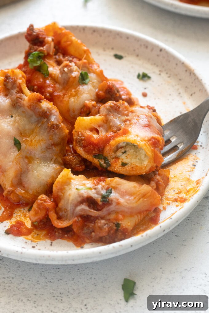 Close-up of a fork digging into a stuffed shell with ground beef, showing the rich filling and sauce.