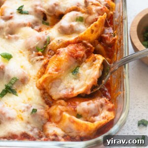 Serving spoon with stuffed shells with ground beef, garnished with fresh basil.