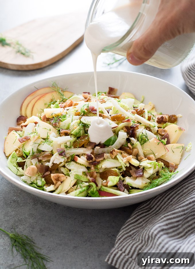 A close-up of Creamy Shaved Brussels Sprout Salad with a generous drizzle of creamy white dressing being poured over it, highlighting its fresh appeal.