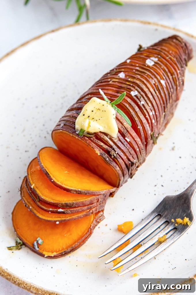 Crispy Hasselback Sweet Potatoes 7 A single rosemary Hasselback sweet potato on a white plate, with a pat of butter melting on top