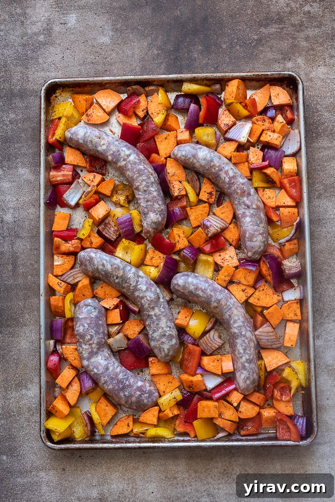 Italian sausage nestled into vegetables on baking sheet.