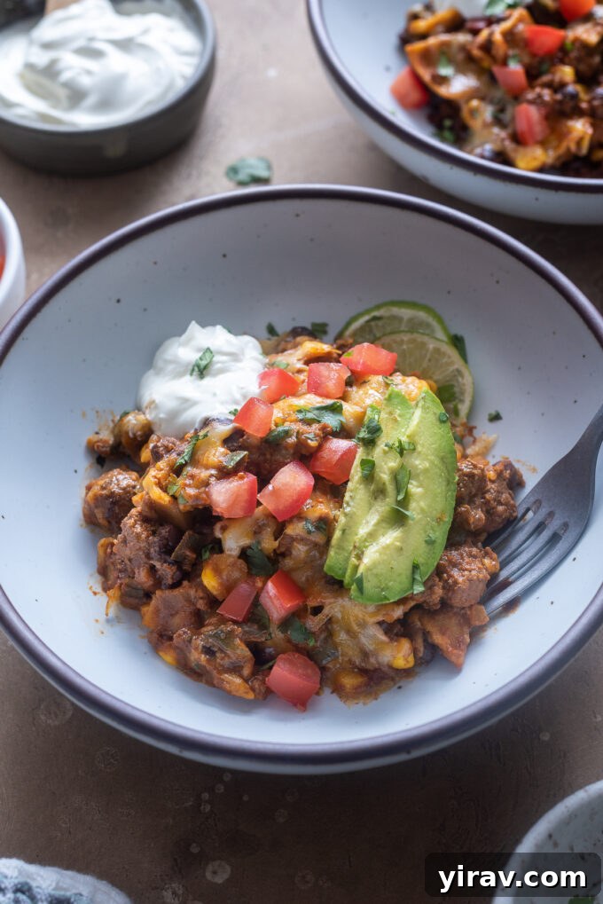 A vibrant serving of skillet enchiladas in a bowl, generously topped with fresh tomato, creamy avocado, and cool sour cream.
