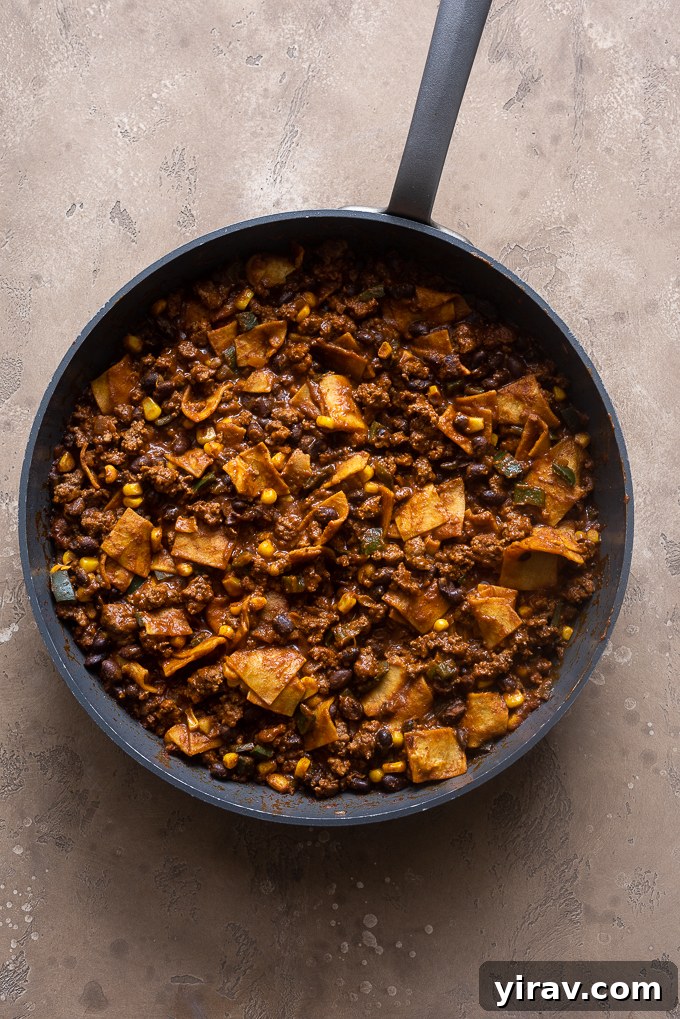 The ground beef enchilada casserole simmering in the skillet, with tortilla pieces absorbing the sauce and thickening.