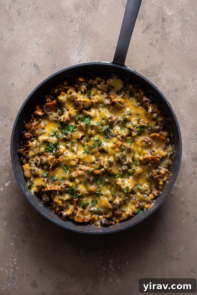 Finished ground beef enchilada casserole in skillet, topped with melted Colby jack cheese and fresh cilantro.