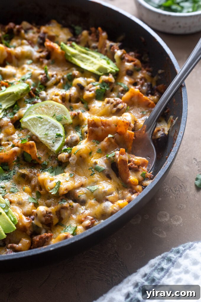 A serving spoon digging into the cheesy ground beef enchilada casserole in the skillet, ready for individual portions.