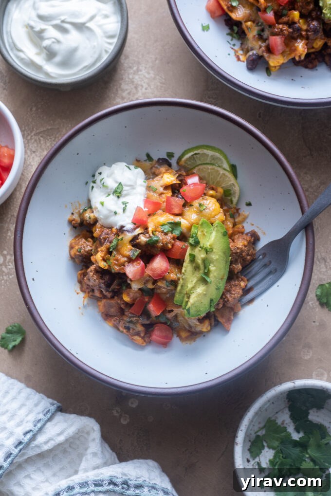 A bowl of ground beef enchiladas skillet, garnished with fresh cilantro, avocado, and a dollop of sour cream.