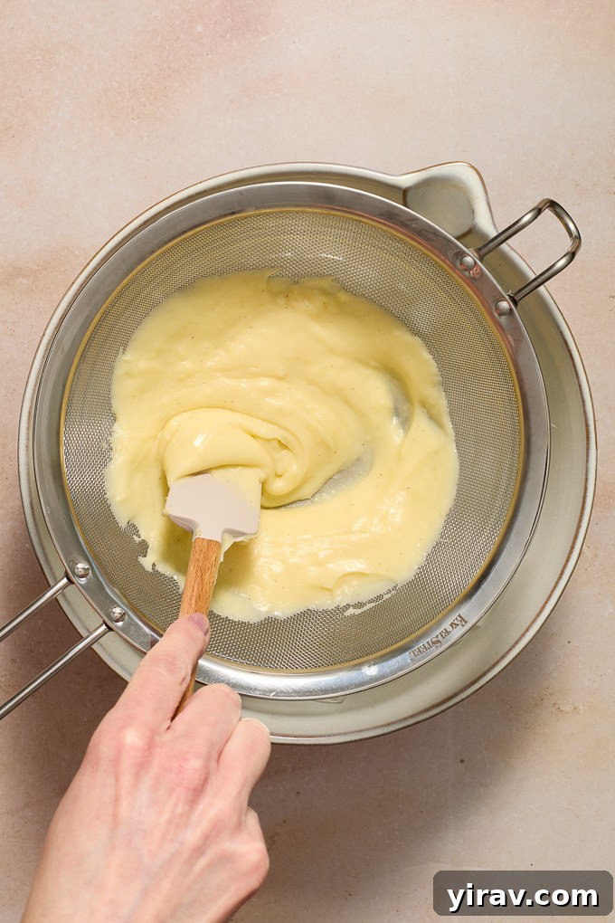 Rubber scraping pushing pastry cream through strainer.