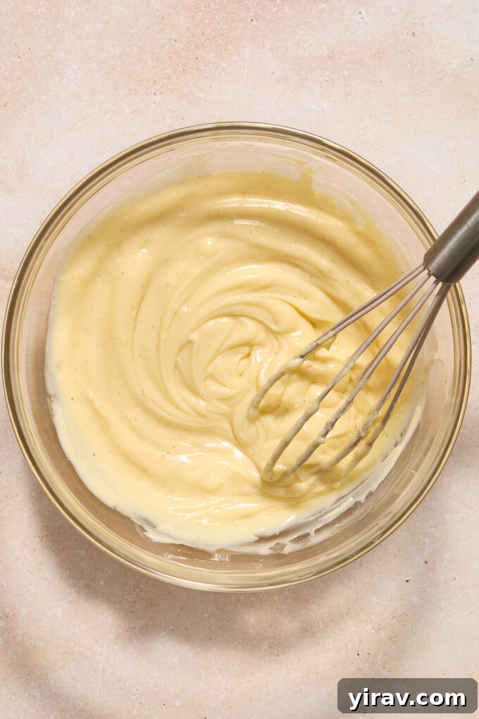 Homemade pastry cream in a mixing bowl with a whisk.