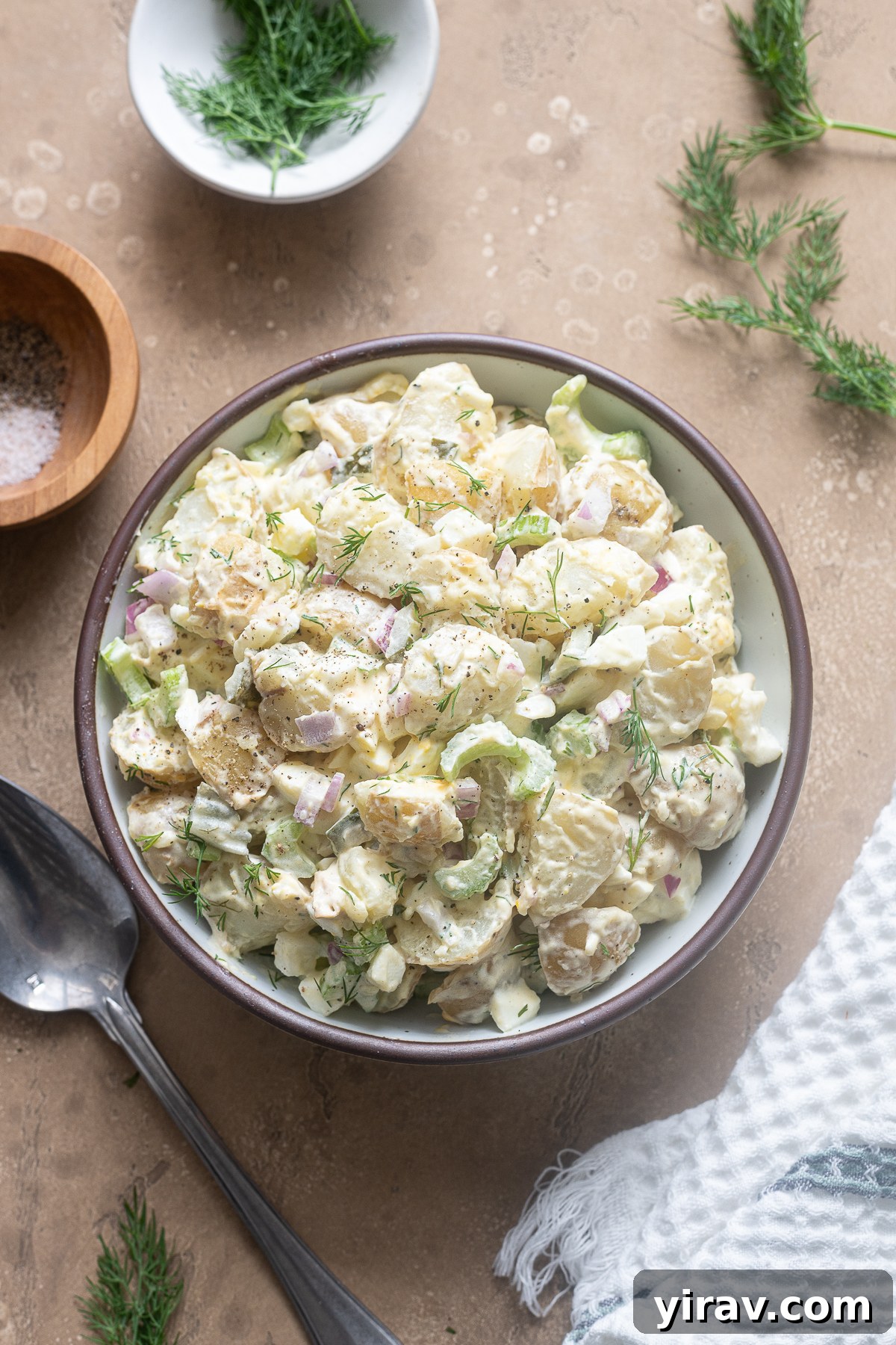 A serving bowl filled with creamy Dill Pickle Potato Salad, garnished with fresh dill.