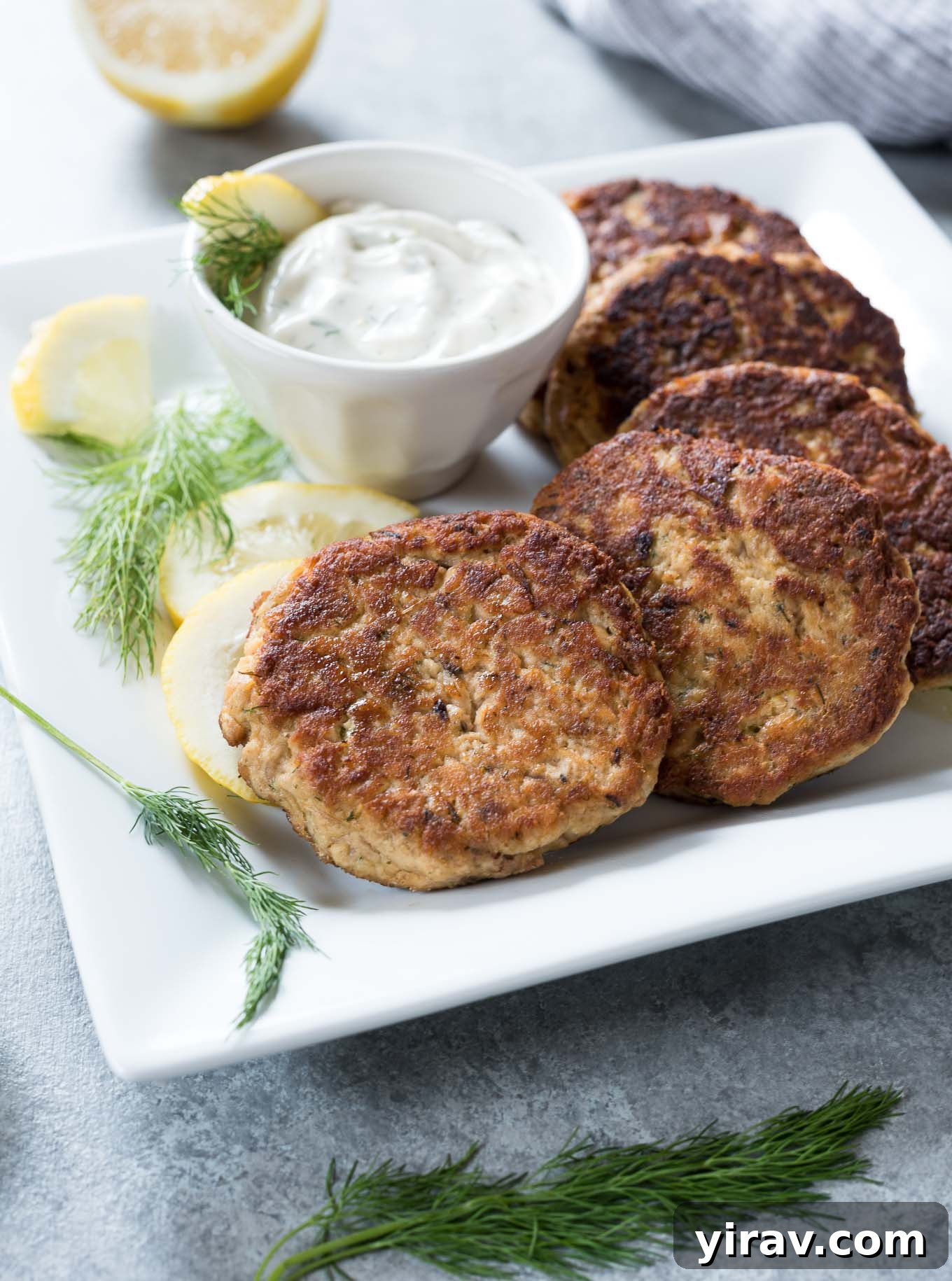 Crispy salmon patties elegantly arranged on a platter, served with a delectable lemon dill sauce.