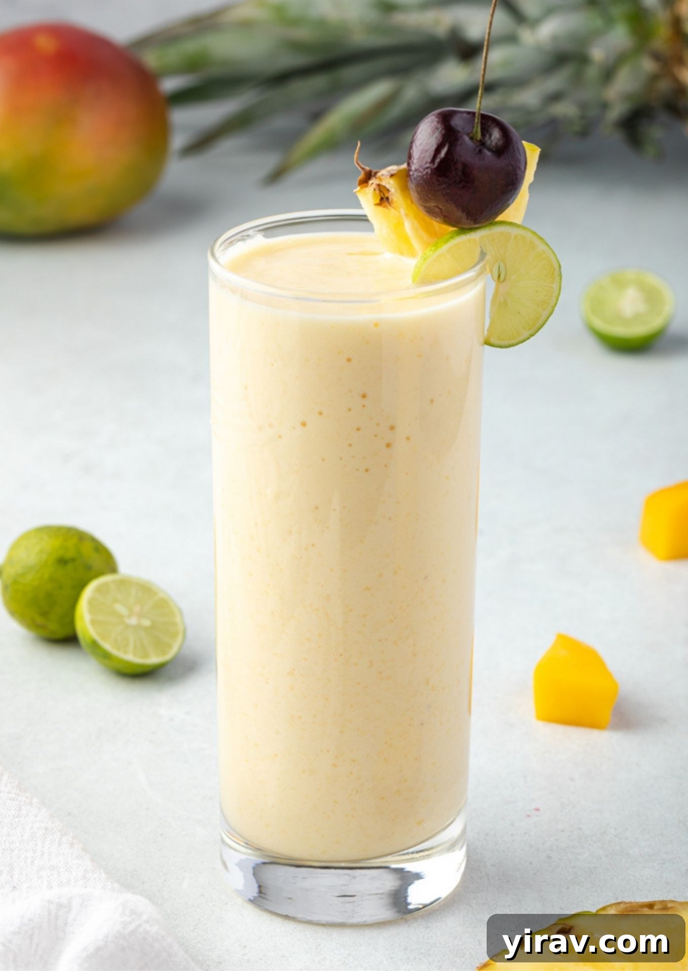 A refreshing Tropical Smoothie, garnished with pineapple, cherry, and a lime slice on the rim, in an elegant glass.