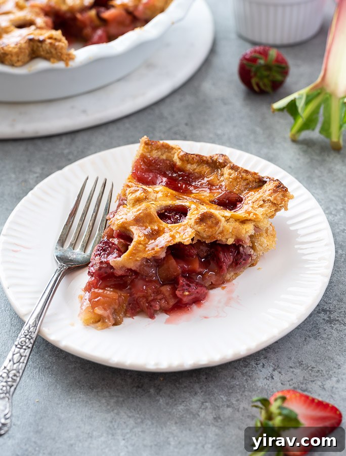 A delectable slice of Strawberry Rhubarb Pie on a plate, with a fork alongside, highlighting its perfect crust and fruity filling.