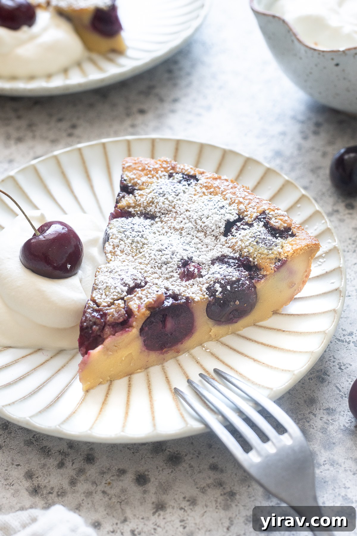 A delightful slice of Cherry Clafoutis on a plate, garnished with a dollop of whipped cream, showcasing its rustic elegance.