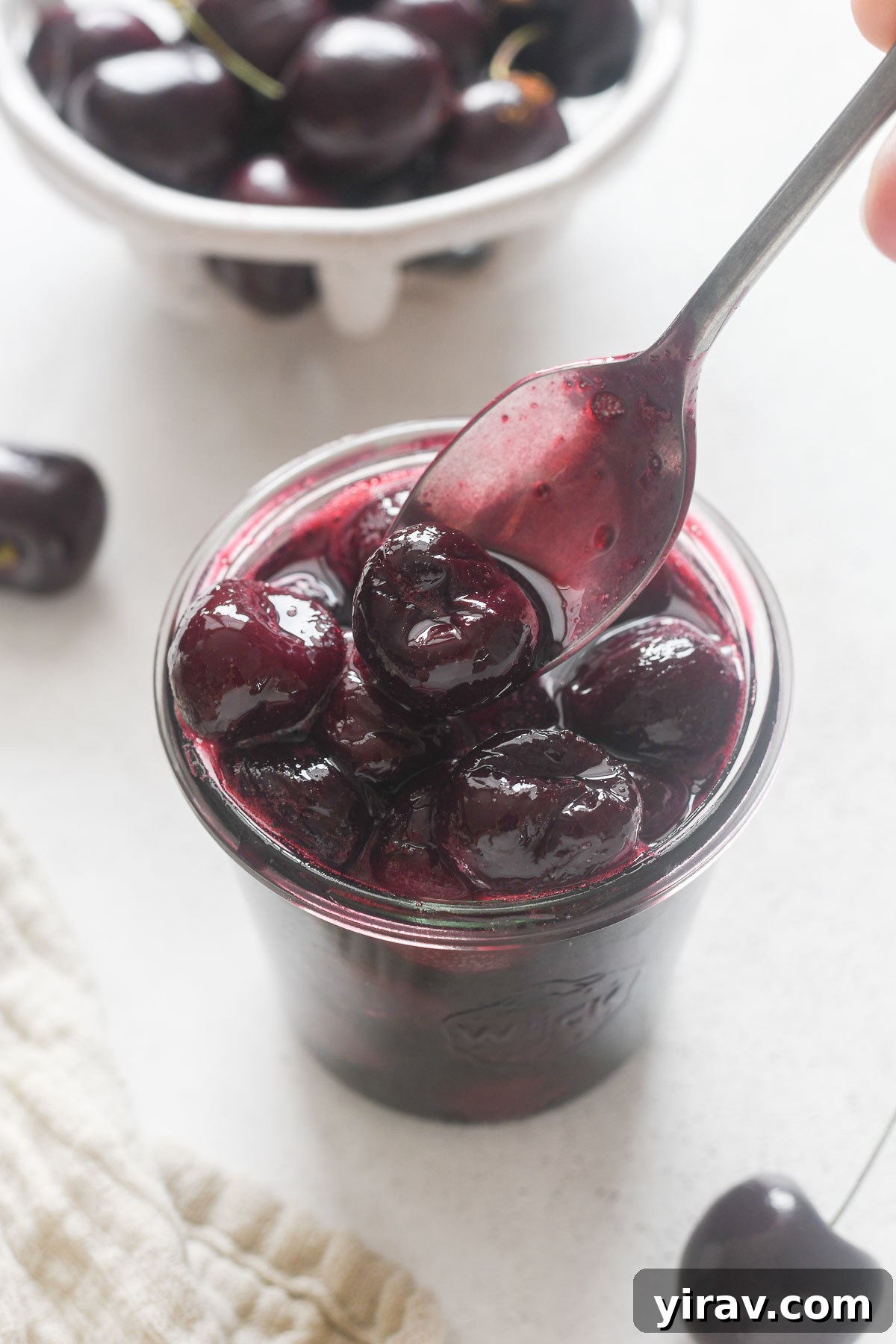 A spoonful of glistening Cherry Compote delicately drizzled over a jar, ready to be enjoyed as a topping.