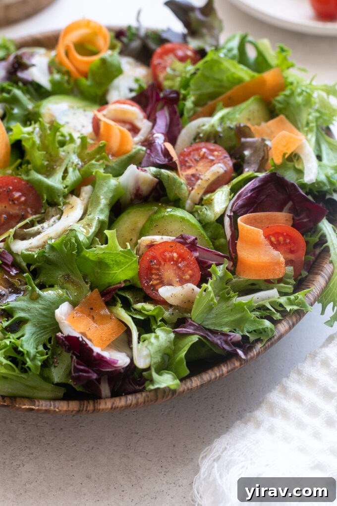 Close-up of Insalata Mista featuring finely sliced fennel, halved cherry tomatoes, and various green leaves, generously coated in balsamic dressing.