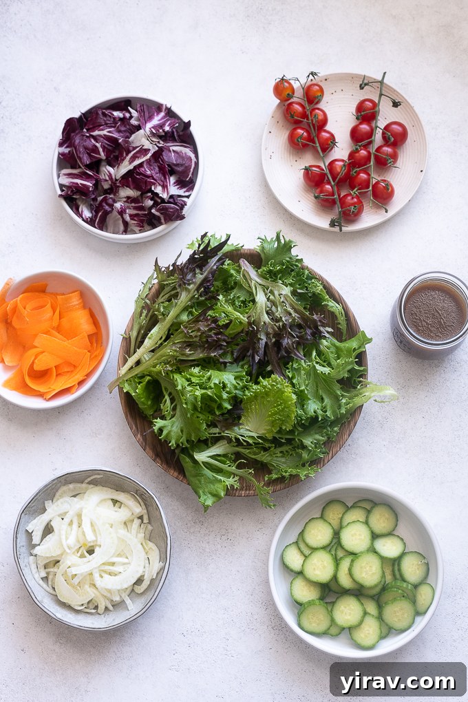 Freshly washed and chopped ingredients for Insalata Mista arranged on a cutting board, including mixed greens, radicchio, fennel, carrots, tomatoes, and cucumbers.