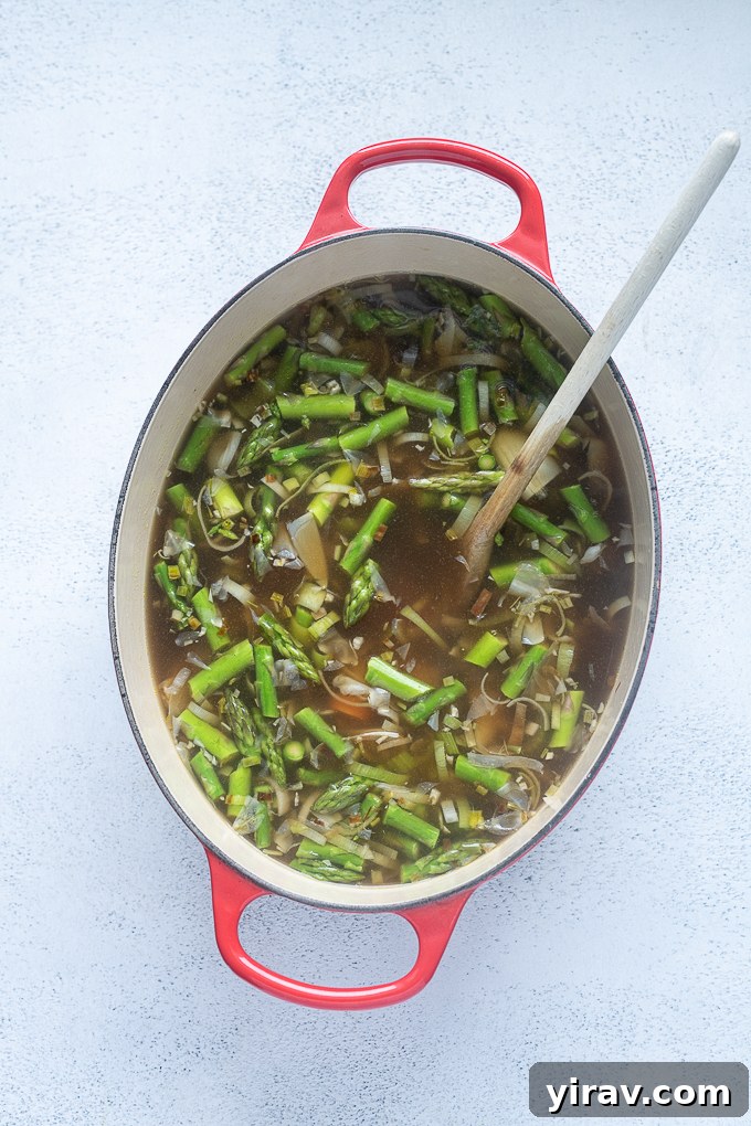Fresh Spring Harvest Soup 6 Vegetable stock added to aromatics, with asparagus and white beans, simmering.
