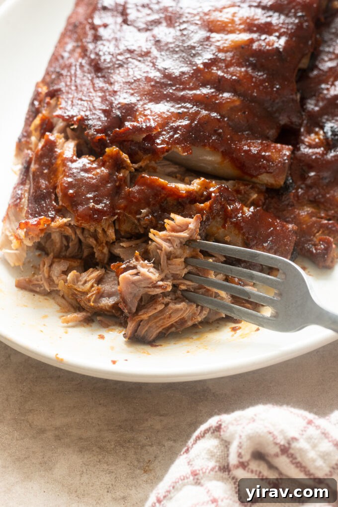 Slow cooked BBQ baby back ribs on a platter with fork pulling them apart.