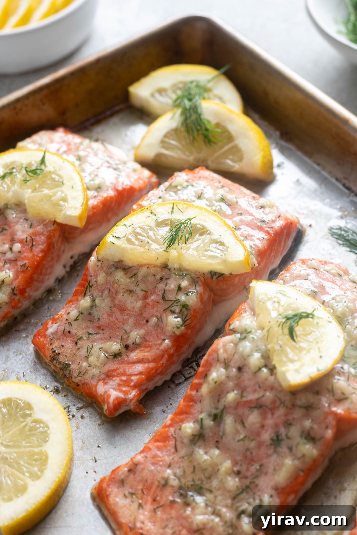 Garlic butter salmon on a baking sheet with dill and lemon.