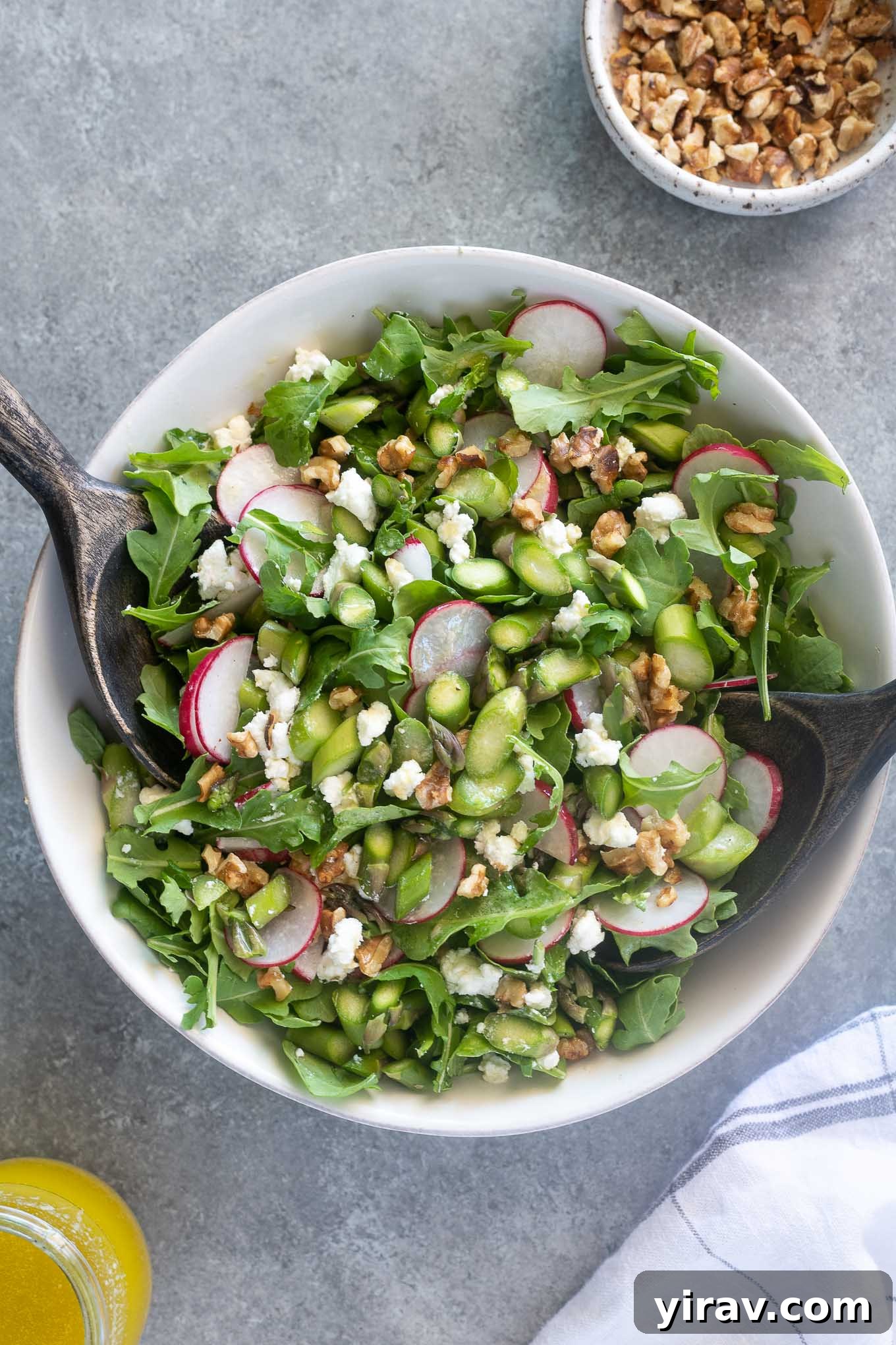 Asparagus salad in a white bowl with salad servers digging in