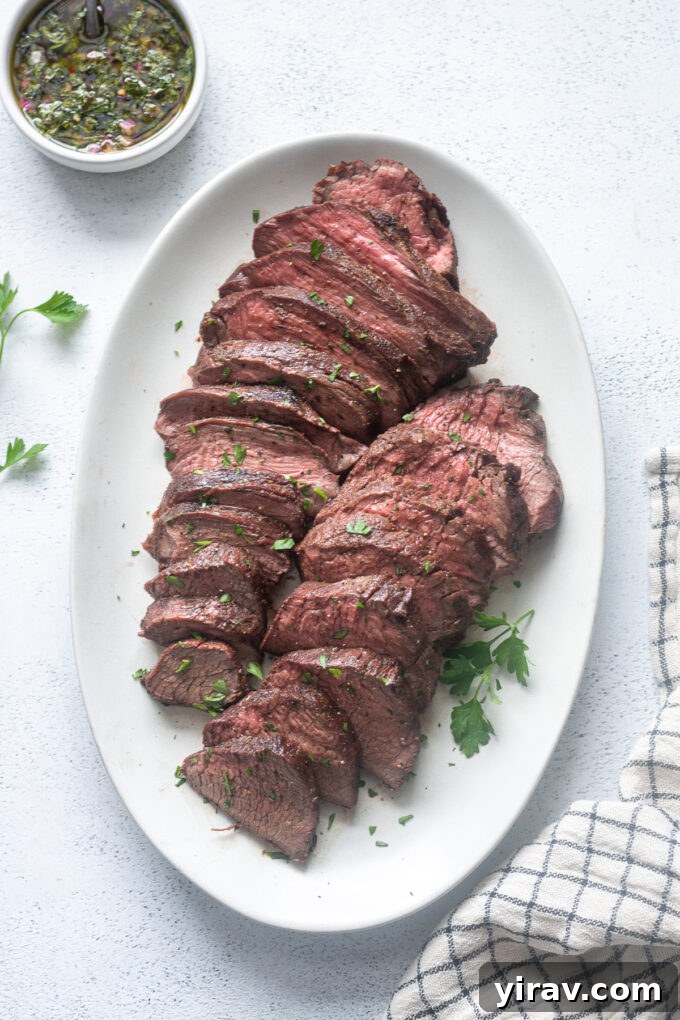 Juicy, sliced grilled beef tri tip roast garnished with fresh parsley on a white serving platter.