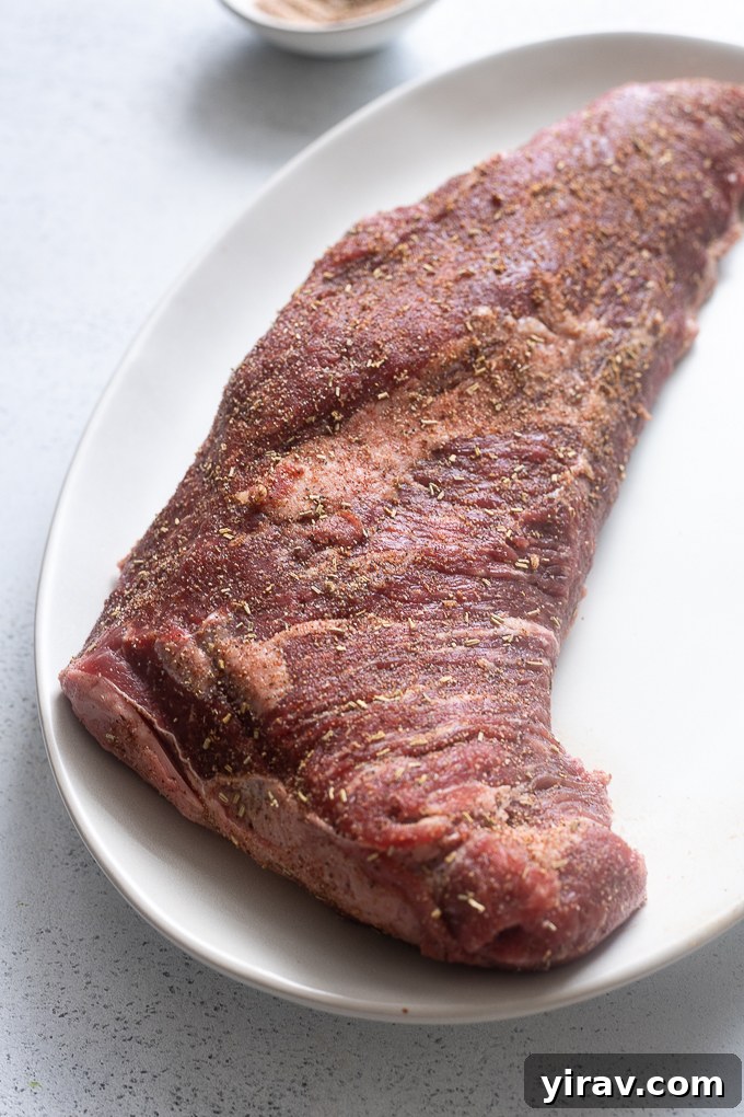 Generously seasoning beef tri tip roast with Santa Maria rub on a platter, ready for grilling.
