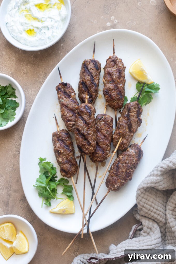 Close-up of grilled lamb kofta on a platter, garnished with lemon and cilantro.