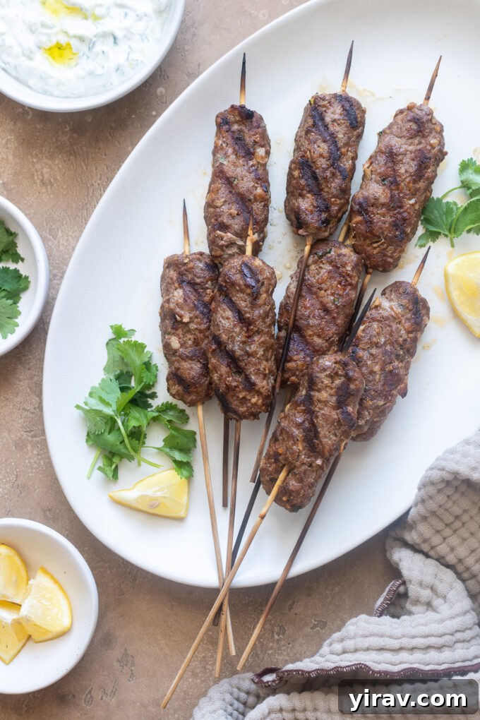 Grilled lamb kofta kebabs presented on a serving platter with fresh herbs and lemon wedges.