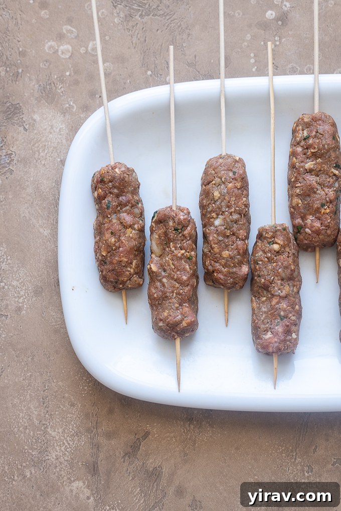 Oblong lamb kofta logs skewered on wooden sticks, brushed with oil.