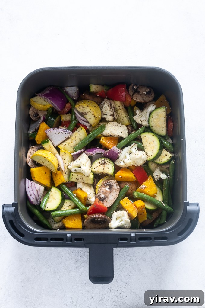 Seasoned vegetables arranged in a single layer in the air fryer basket before cooking.