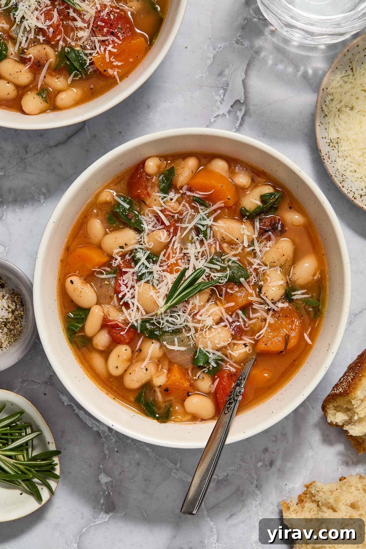 Bowl of vegetarian white bean stew topped with rosemary and parmesan.