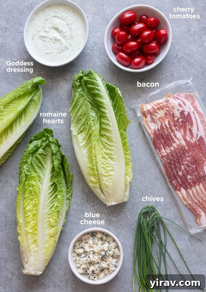 A flat lay of all the fresh ingredients needed for the Romaine Wedge Salad recipe, including romaine hearts, cherry tomatoes, blue cheese, bacon, and chives.