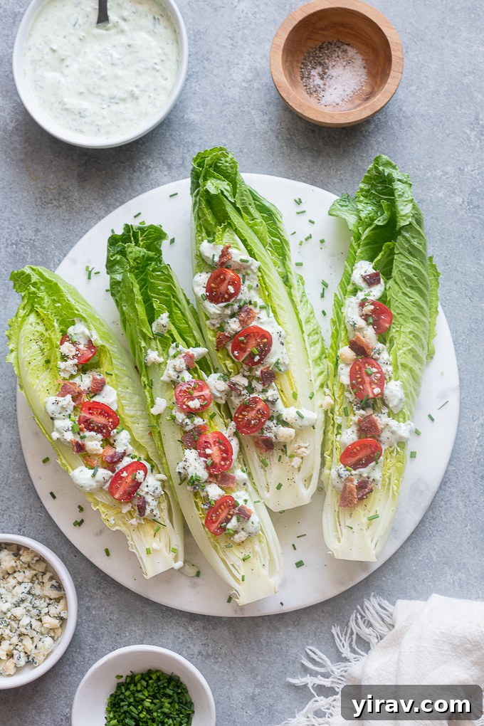 A freshly assembled Romaine Wedge Salad on a platter, featuring halved romaine hearts topped with cherry tomatoes, bacon, blue cheese, and a generous drizzle of Green Goddess dressing.