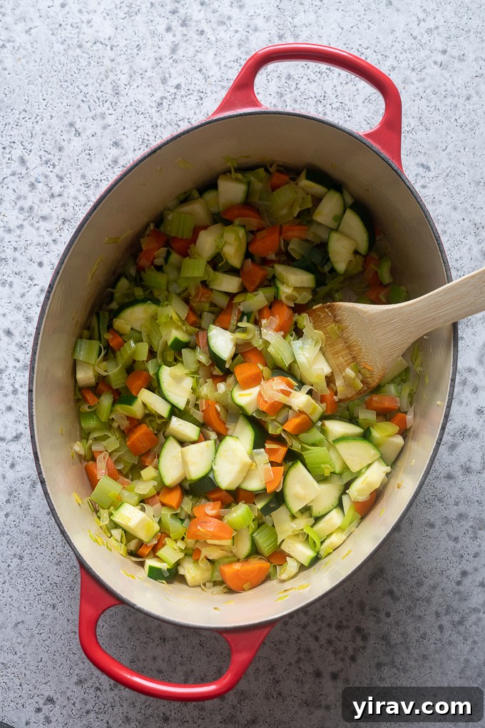 Sautéing aromatics and zucchini for summer vegetable soup with pesto in a pot.