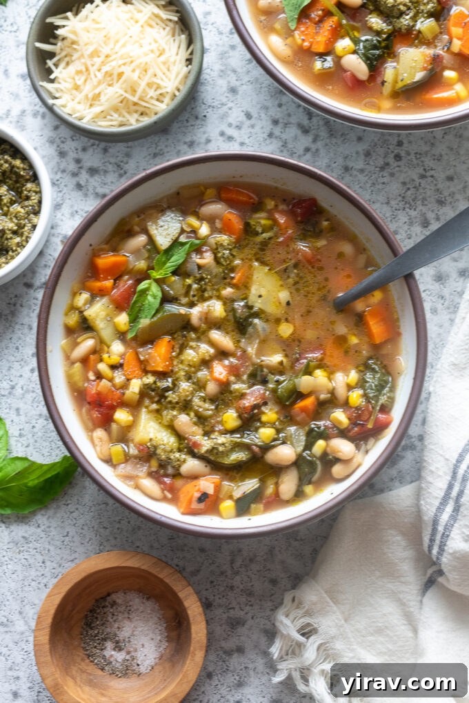 A bowl of Summer Vegetable Soup with Pesto, garnished with a fresh basil sprig.