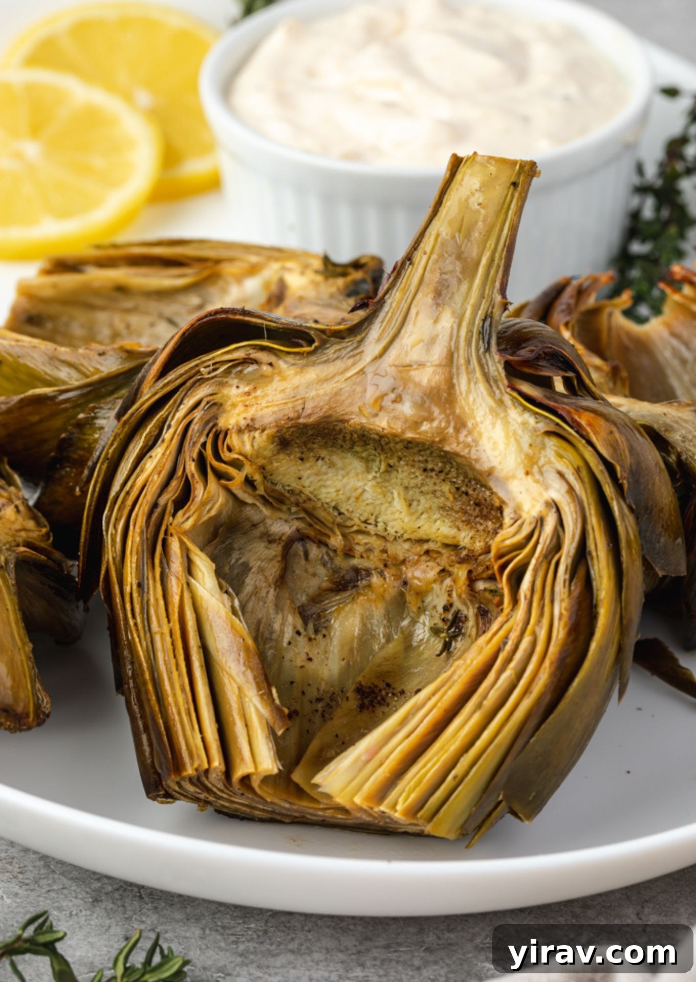 Roasted artichokes on a platter with aioli and lemon