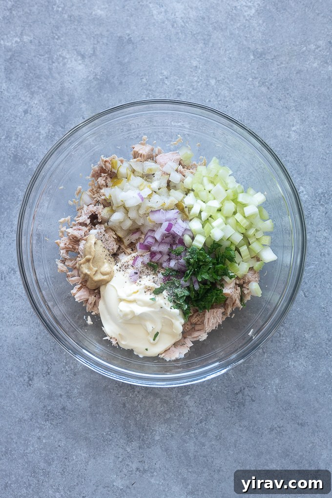 Zesty Dill Pickle Tuna 5 Tuna salad ingredients being mixed in a bowl, with a fork mashing the tuna.