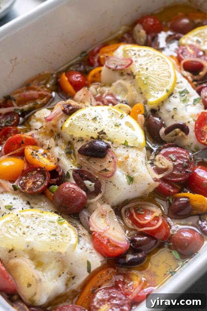 Baked cod with cherry tomatoes, olives, and lemon in a white baking dish.