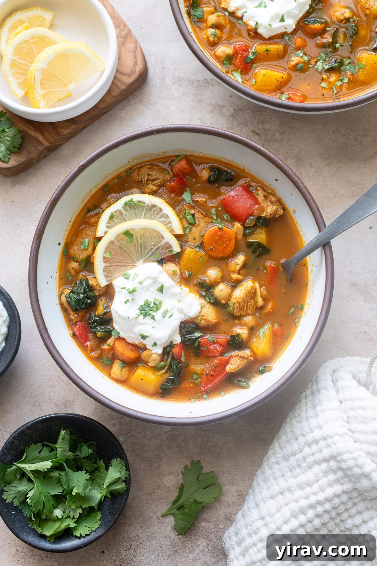 A bowl of Moroccan chicken soup with chickpeas, garnished with lemon and Greek yogurt.