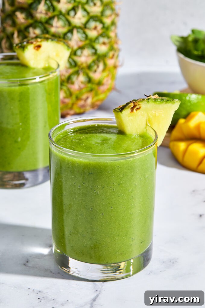 Tropical Green Power Smoothie 2 A vibrant green tropical mango kale smoothie in a tall glass, garnished with a pineapple wedge.