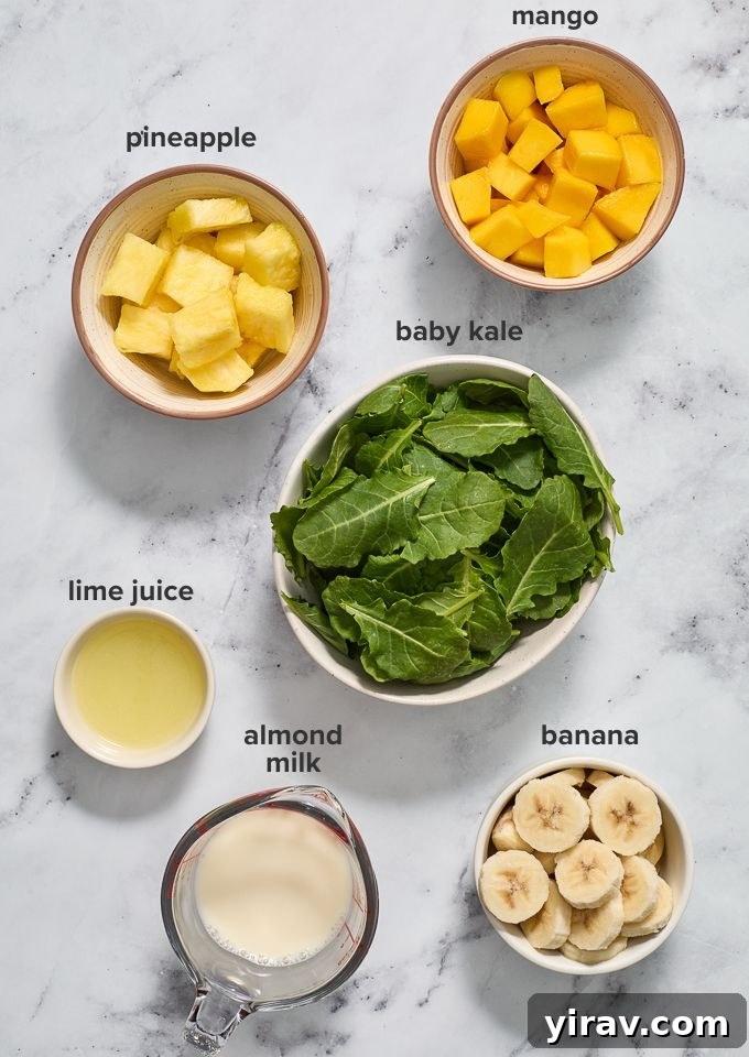 Tropical Green Power Smoothie 4 A collection of fresh ingredients laid out for a kale smoothie recipe: kale, mango, pineapple, banana, lime, and almond milk.