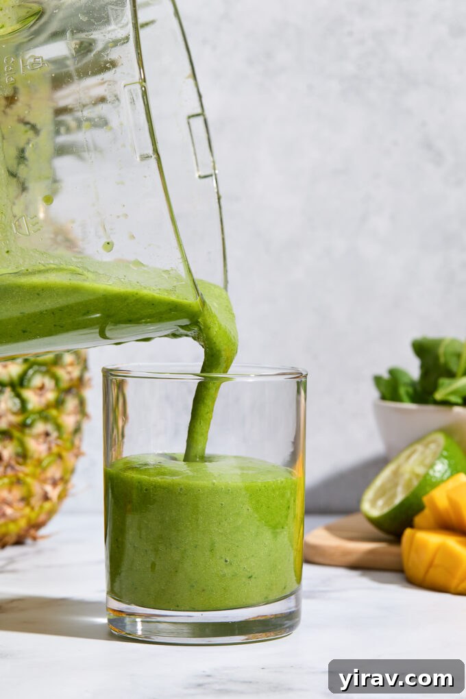 Tropical Green Power Smoothie 6 A delicious and healthy kale and fruit smoothie being poured from a blender into a glass, highlighting its rich green color and smooth texture.