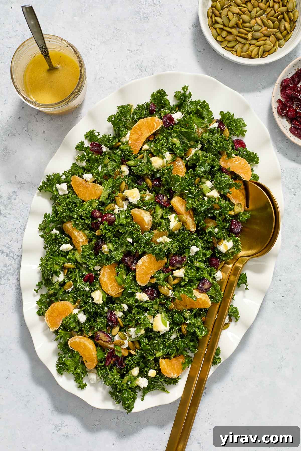 Kale salad with goat cheese on a platter with salad servers.