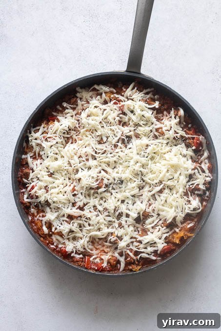 Spaghetti squash casserole in skillet before baking, with cheese on top.