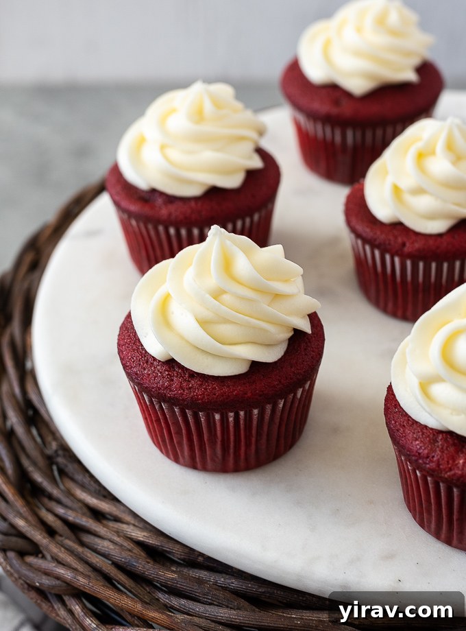 A tantalizing display of red velvet cupcakes, generously topped with creamy white frosting, arranged on a chic marble serving board, highlighting their vibrant color and inviting texture.
