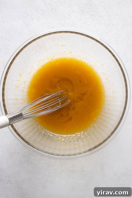 Wet ingredients for almond flour lemon loaf cake, including eggs, maple syrup, olive oil, and lemon, ready to be whisked.