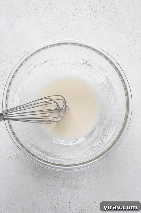 A small bowl containing the ingredients for the lemon glaze, including powdered sugar and lemon juice, ready for whisking.