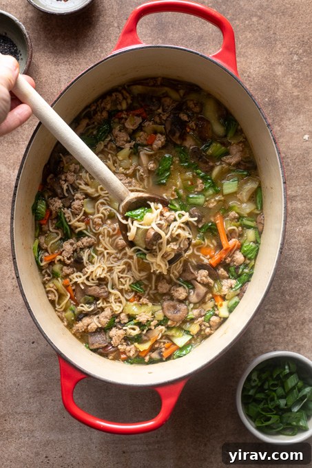 Homemade ramen with ground pork in Dutch oven with wooden spoon.