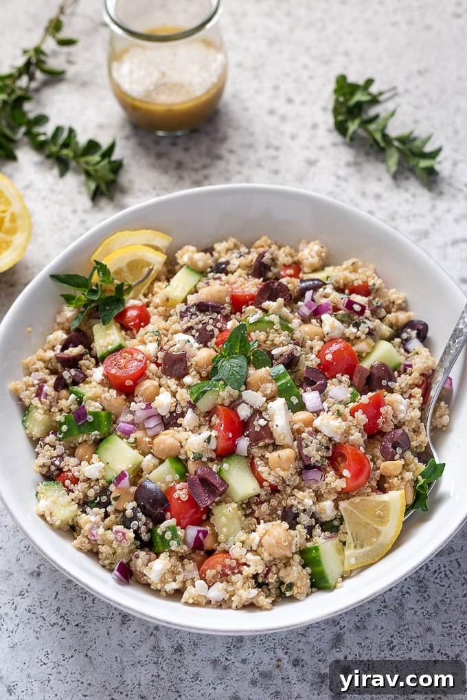A close-up of a large serving bowl filled with Greek quinoa salad, with a spoon nestled amongst the colorful ingredients, ready to be served.